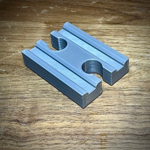 May include: A gray plastic train track piece with two holes for connecting to other tracks.