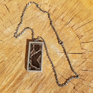 May include: A silver chain necklace with a rectangular pendant featuring a brown and black snakeskin pattern.