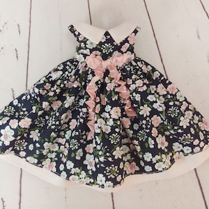 May include: A black and white floral dress with a pink ribbon bow and a white collar. The dress has a full skirt and is made of a lightweight fabric.