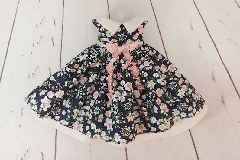 May include: A black and white floral dress with a pink ribbon bow and a white collar. The dress has a full skirt and is made of a lightweight fabric.