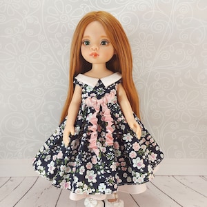 May include: A doll with long red hair wearing a blue and white floral dress with a pink bow. The doll is wearing white shoes with a pink bow.