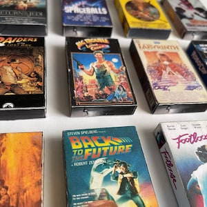 May include: A collection of vintage VHS tapes featuring popular movies from the 1980s, including "Return of the Jedi", "Spaceballs", "Raiders of the Lost Ark", "Big Trouble in Little China", "Labyrinth", "Robocop", "Back to the Future", and "Footloose".