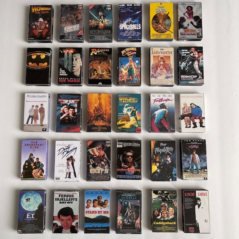 May include: A collection of VHS tapes featuring various movie titles, including "Howard the Duck", "Empire Strikes Back", "Spaceballs", "Die Hard", "Raiders of the Lost Ark", "The Breakfast Club", "Rocky IV", "The Terminator", "Ferris Bueller's Day Off", "Stand By Me", "E.T. the Extra-Terrestrial", "Caddyshack", and more.