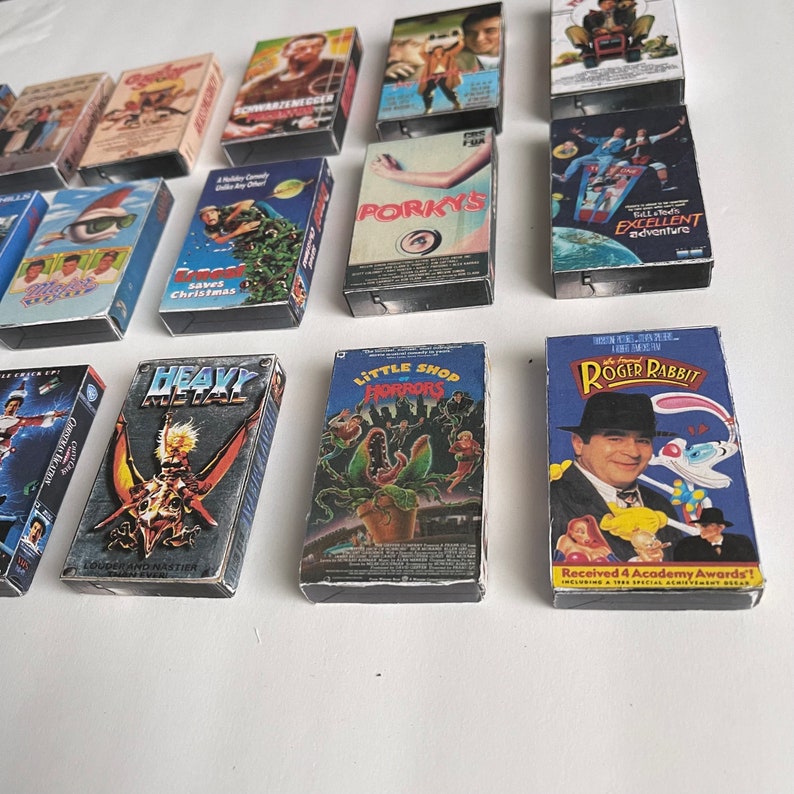 May include: A collection of VHS tapes featuring various movie titles, including "Schwarzenegger", "Porky's", "Heavy Metal", "Little Shop of Horrors", and "Roger Rabbit".
