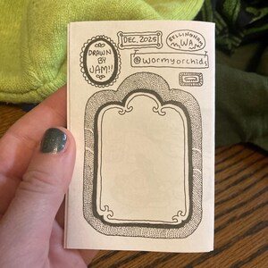 Puede incluir: Un peque&ntilde;o folleto dibujado a mano con un marco decorativo y el texto "DRAWN BY JAM!!" y "DEC. 2025". El texto adicional incluye "@wormyorchids" y "Bellingham WA". El folleto est&aacute; sostenido por una persona.