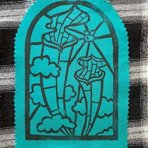 May include: A teal fabric patch with pinked edges featuring a black screen-printed design of two pitcher plants inside an arched window frame. The illustration includes stylised clouds and a sun, mimicking the appearance of a stained glass window.