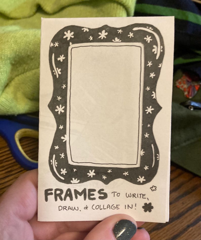 Puede incluir: Un marco de papel rectangular con un borde negro decorado con peque&ntilde;as flores blancas en forma de estrella. El texto "FRAMES TO WRITE, DRAW, & COLLAGE IN!" est&aacute; impreso en la parte inferior del marco. El marco est&aacute; sostenido por una persona.