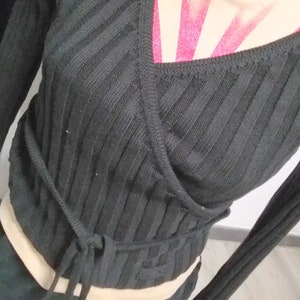 May include: Black ribbed knit wrap top with long sleeves and a tie at the waist. The top features a small white crown logo on the right side.