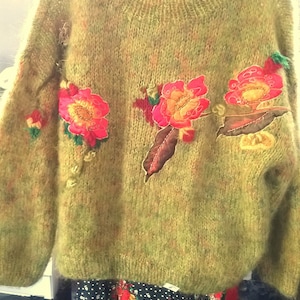 May include: A green fuzzy sweater with embroidered flowers in shades of red, yellow, and brown.