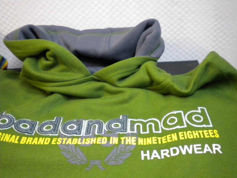 May include: Green hooded sweatshirt with the text "badandmad" in white and yellow lettering. The text "ORIGINAL BRAND ESTABLISHED IN THE NINETEEN EIGHTIES HARDWEAR" is also printed on the sweatshirt.