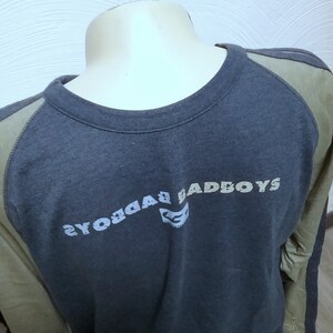 May include: A dark blue long-sleeved shirt with a green and white color block design. The shirt has a crew neck and the text "BADBOYS" printed on the front in a white and gray font.