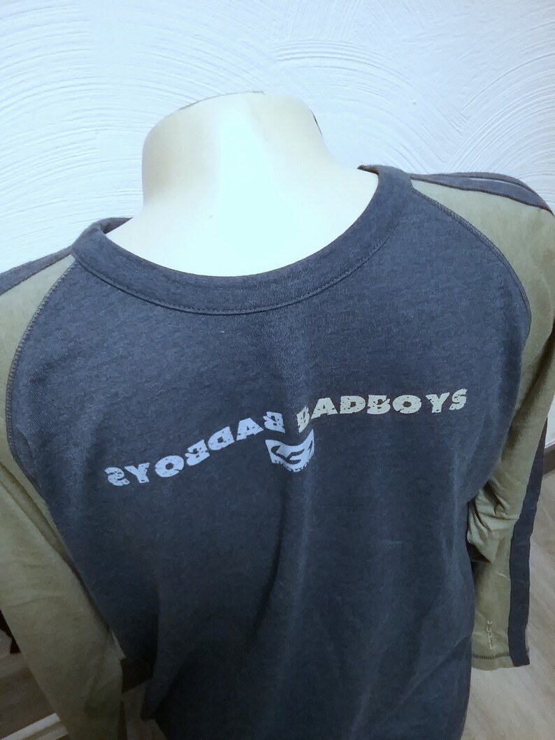 May include: A dark blue long-sleeved shirt with a green and white color block design. The shirt has a crew neck and the text "BADBOYS" printed on the front in a white and gray font.