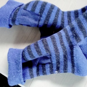 May include: A pair of fingerless gloves featuring a horizontal striped pattern in shades of blue and dark gray. The gloves have a ribbed cuff at the wrist and a dedicated opening for the thumb, constructed from a knit fabric with a textured finish.