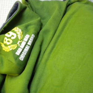 May include: Green hooded sweatshirt with a white embroidered logo that says "Bad and Mad Original Brand" and a yellow laurel wreath with the number "89" inside.
