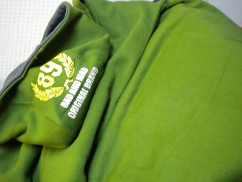 May include: Green hooded sweatshirt with a white embroidered logo that says "Bad and Mad Original Brand" and a yellow laurel wreath with the number "89" inside.
