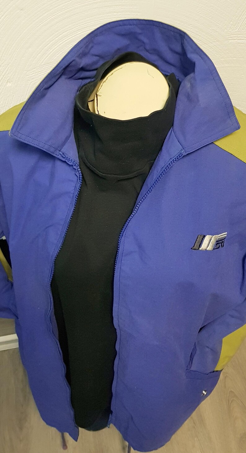 May include: A blue and yellow vintage jacket with a black turtleneck underneath. The jacket has a zipper closure and a logo on the chest. The jacket is displayed on a mannequin.