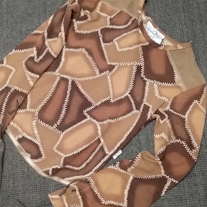 May include: A brown long-sleeved shirt with a patchwork design. The shirt has a brown and white geometric pattern with stitching details. The shirt has a drawstring at the bottom of each sleeve.
