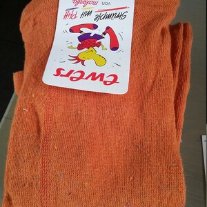 May include: Orange cotton socks with a white tag that says "Schrumpfe mit Pfiff!" and "von Modelefa" with a cartoon illustration of a person doing a handstand. The tag also says "GWEIS" and "6026 S. Größe 125-164"