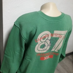 May include: Green sweatshirt with a white and red graphic print that says "Camard Rescue 87 Training Camp XXL".