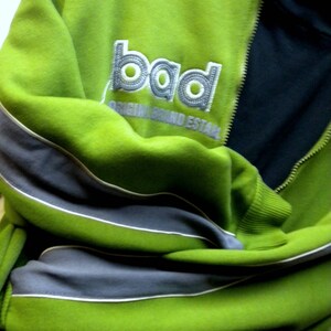 May include: Green and gray zippered jacket with a white embroidered logo that says "bad original brand establ"
