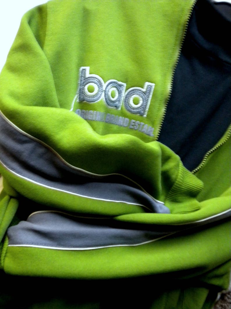 May include: Green and gray zippered jacket with a white embroidered logo that says "bad original brand establ"