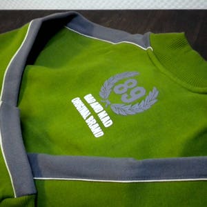 May include: Green sweatshirt with a gray trim and a white logo that says "Go and Mad Original Brand" with a laurel wreath and the number "89" in the center.