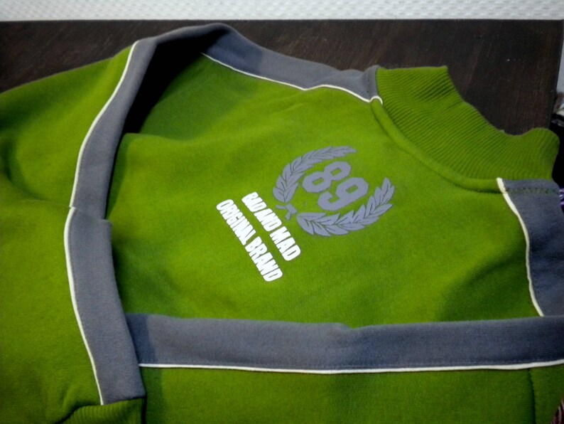 May include: Green sweatshirt with a gray trim and a white logo that says "Go and Mad Original Brand" with a laurel wreath and the number "89" in the center.