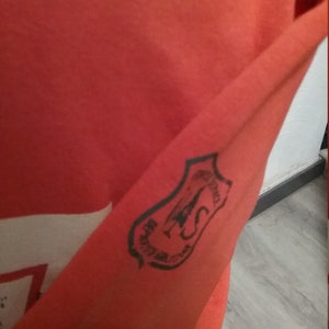 May include: Orange long-sleeve shirt with a black and white patch on the sleeve. The patch features a plane and the text "TOWING SERVICE".