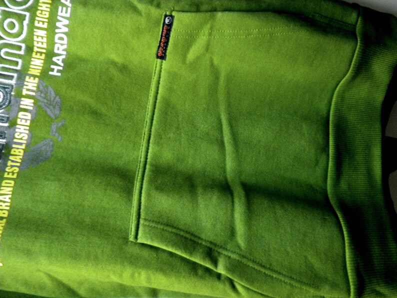 May include: Green hooded sweatshirt with a large graphic print on the front. The print includes the text "Original Brand Established in the Nineteen Eighty" and "Hardware". The sweatshirt has a kangaroo pocket on the front.