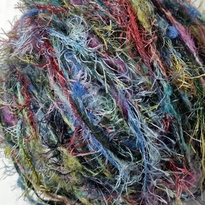 Puede incluir: Primer plano de una madeja de hilo colorido. El hilo es una mezcla de azules, verdes, rojos y morados, con un aspecto difuso y texturizado. El hilo parece estar hecho de múltiples hebras, creando un aspecto grueso y texturizado. Ideal para proyectos de tejido y ganchillo.