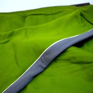 May include: A green sweater with a gray trim around the edges. The sweater is folded in half and the trim is visible on the outside of the fold.