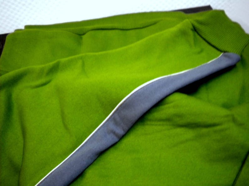 May include: A green sweater with a gray trim around the edges. The sweater is folded in half and the trim is visible on the outside of the fold.
