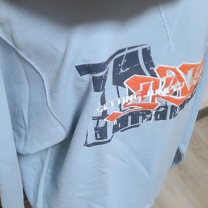 May include: A light blue hooded sweatshirt with a graphic print of a basketball hoop and the text "Getting Juicy" in orange and black.