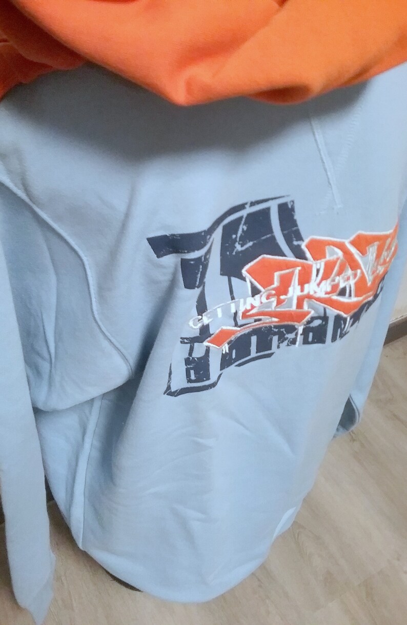 May include: A light blue hooded sweatshirt with a graphic print of a basketball hoop and the text "Getting Juicy" in orange and black.