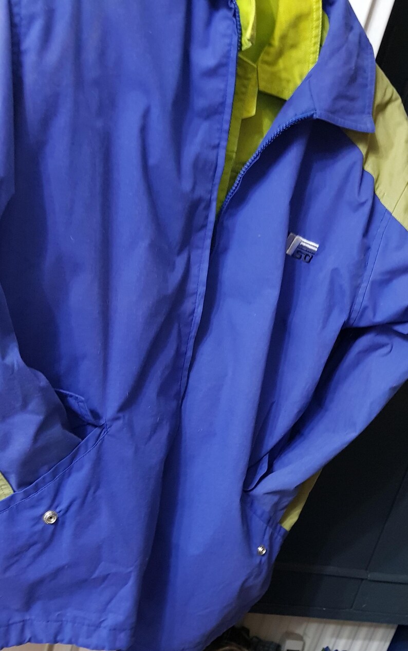 May include: A blue and green jacket with a zipper closure. The jacket has a logo on the chest and two pockets. The interior lining is green. The jacket is made of a lightweight material.