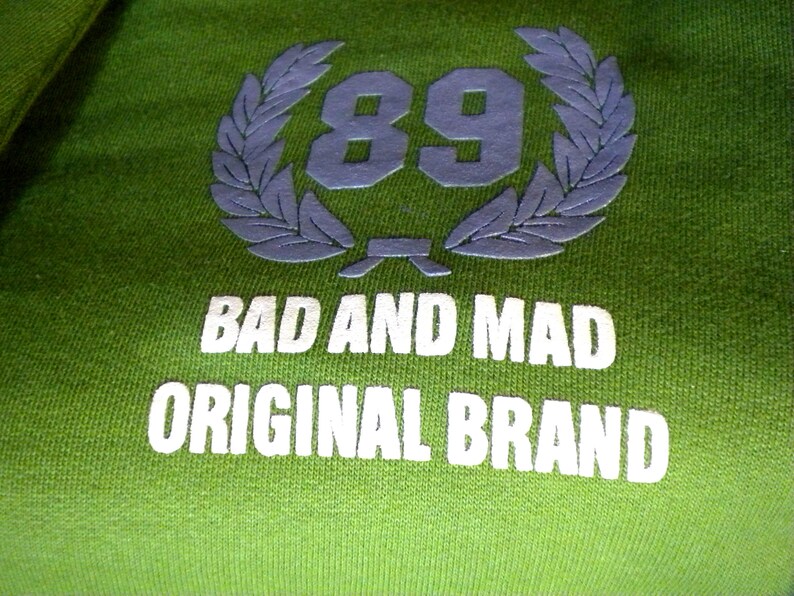 May include: Green sweatshirt with a white logo that says "Bad and Mad Original Brand" and a laurel wreath with the number 89 in the center.