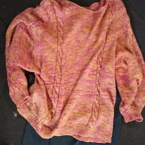 May include: A pink and yellow knitted sweater with a cable knit design. The sweater has long sleeves and a relaxed fit.