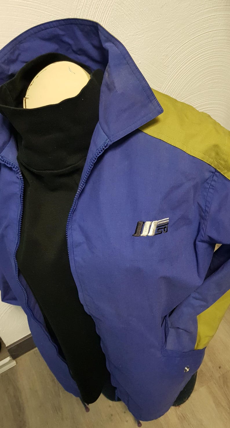 May include: A blue and yellow vintage jacket with a black turtleneck underneath. The jacket has a zipper closure and a small logo on the chest. The jacket is made of a lightweight material.