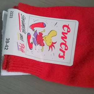 May include: A pair of bright red socks with a white cardboard tag attached. The tag features the brand name Ewers in red script, the text Strümpfe mit Pfiff, the number 2223, the size 39-42, and a cartoon illustration of a yellow creature wearing red socks.