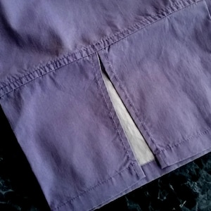 May include: Close-up of a section of lavender fabric, showing a split seam. The fabric has visible stitching and a slight sheen. The background is a dark, marbled surface.