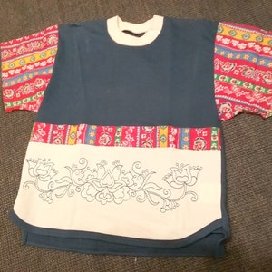 May include: A blue and white t-shirt with a floral pattern on the front and colorful patterned sleeves. The shirt has a white collar and a white band around the bottom.