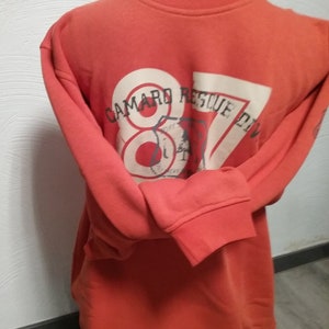 May include: Orange sweatshirt with a white graphic on the back that says "Camard Rescue Div" with a red circle and the number 87 inside.