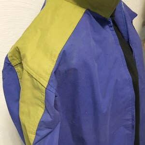 May include: A blue and yellow jacket with a black collar. The jacket has a zipper closure and a pocket. The jacket is made of a lightweight material. The jacket is a casual style.