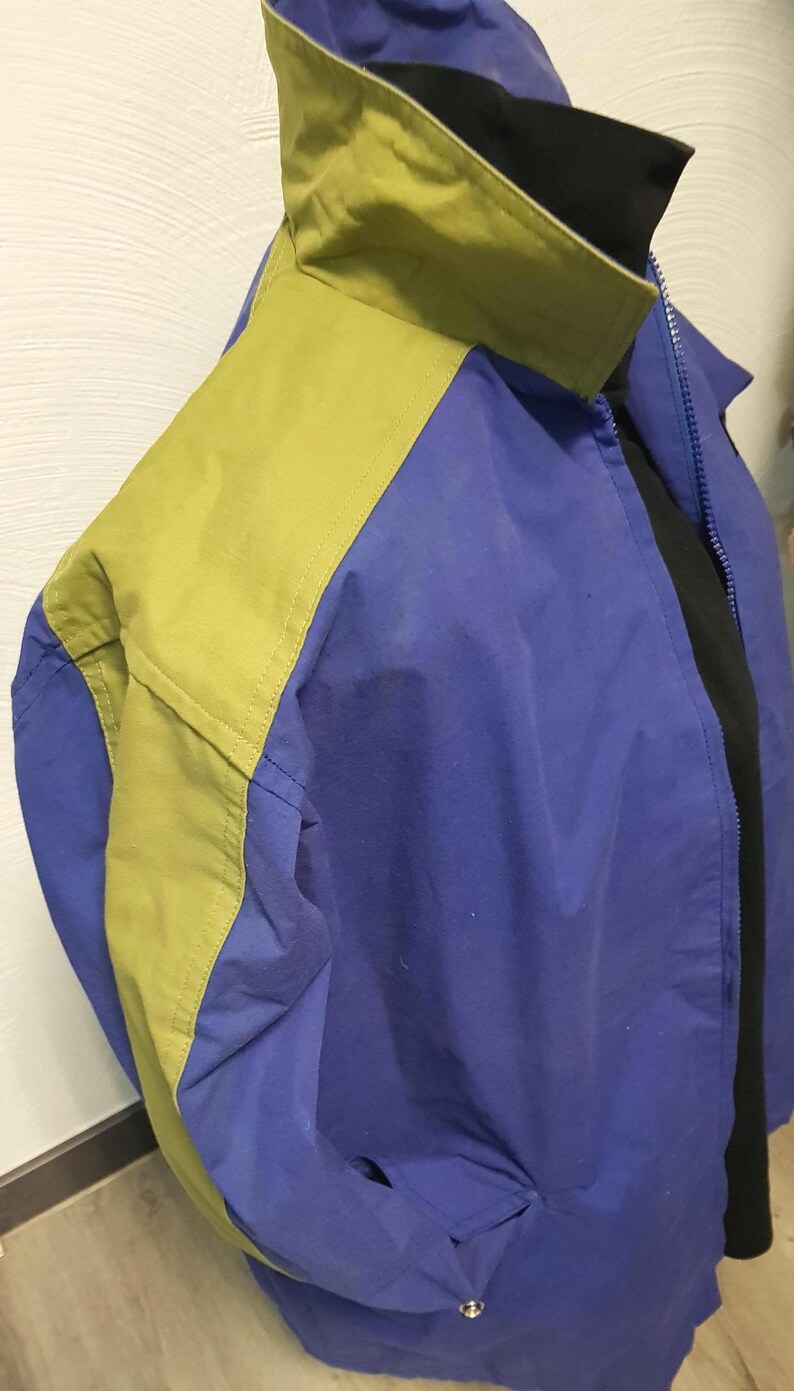 May include: A blue and yellow jacket with a black collar. The jacket has a zipper closure and a pocket. The jacket is made of a lightweight material. The jacket is a casual style.