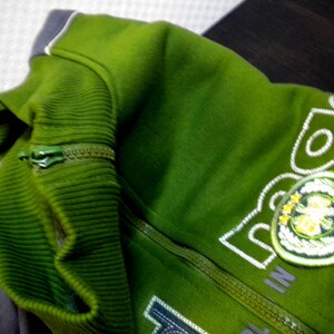 May include: A green zippered jacket with a white embroidered logo that says "TEEN" and has a green and white leaf design.