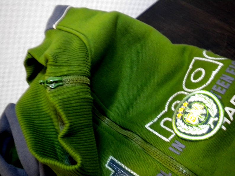 May include: A green zippered jacket with a white embroidered logo that says "TEEN" and has a green and white leaf design.
