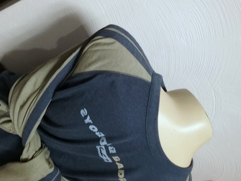 May include: A long-sleeved shirt with a dark blue body and olive green sleeves. The sleeves have a white stripe down the side. The shirt has a graphic print on the front that says "BADBOYS" and "2YOYO's".