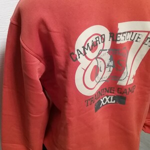 May include: Red sweatshirt with a white graphic print of "Camaro Rescue 87" with a smaller graphic of a tree and the text "Training Camp XXL".