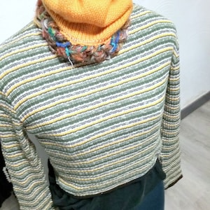 May include: A striped sweater with long sleeves and a yellow knitted beanie. The sweater has a green, white, and yellow striped pattern.