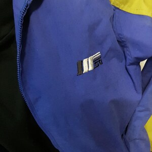 May include: A blue and yellow jacket with a black interior. The jacket has a zipper closure and a small logo on the chest. The collar is blue, and the shoulders are yellow.